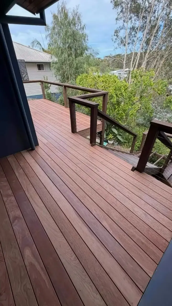 A timber deck with a post-and-rail balustrade and a stair leading down, trees and rooftops beyond.