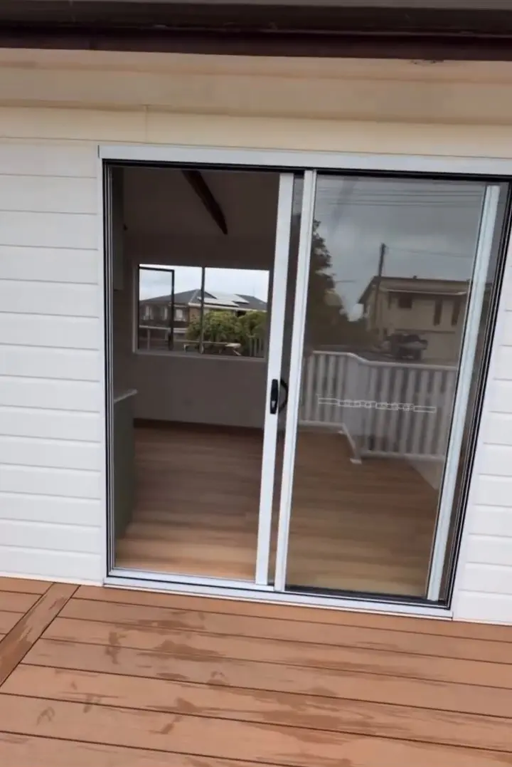 A sliding glass door in a white weatherboard wall, seen from the deck, opening into a room with a timber-look floor.