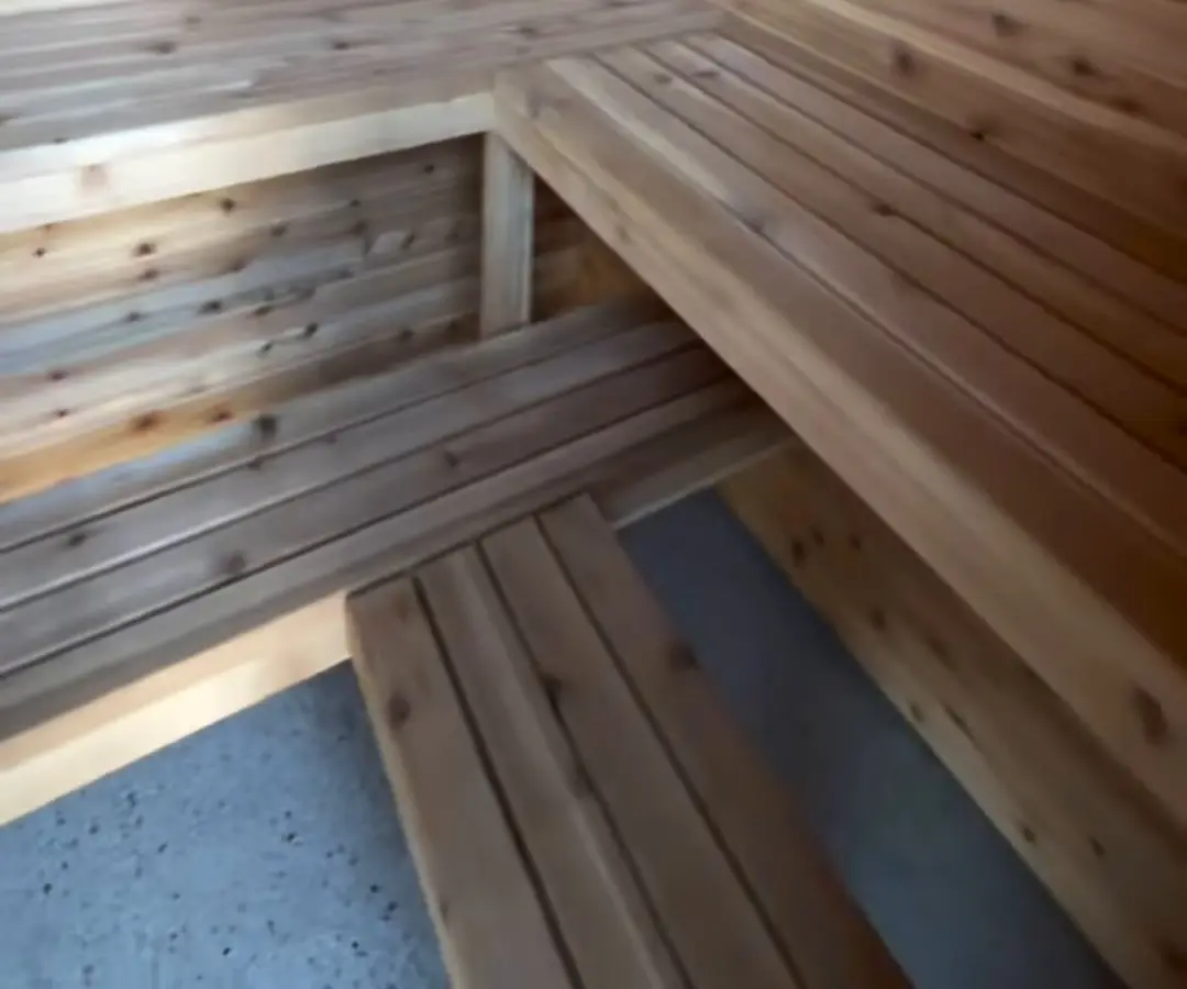 Two tiers of slatted timber benches along a timber-lined wall, over a speckled concrete floor.